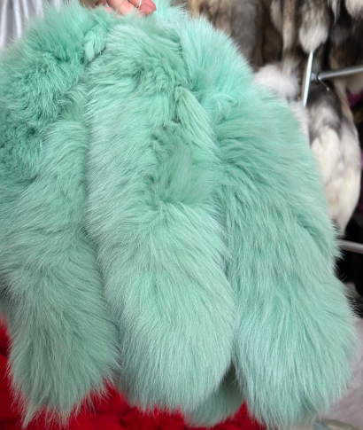 Close-up of a seafoam green fur tail held by a hand against a blurred background.